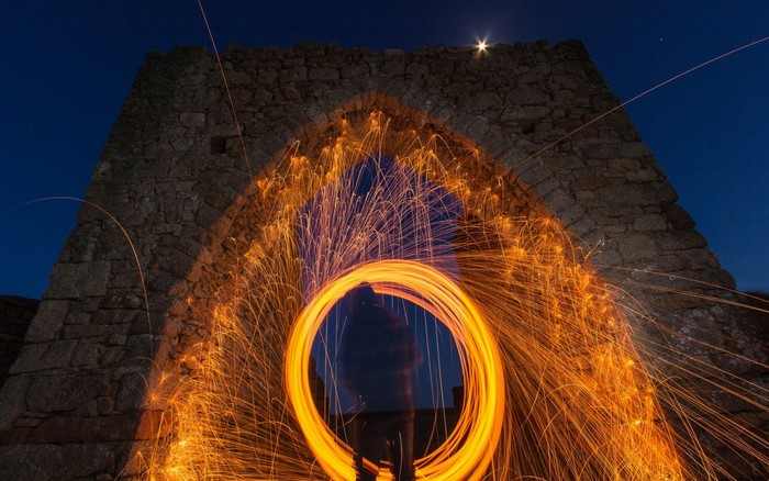 Person creating light painting with sparks under stone arch at night