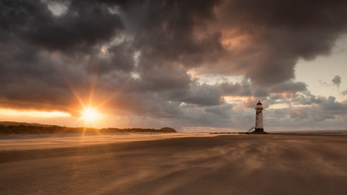 Lighthouse on a sandy beach at sunset with dramatic clouds