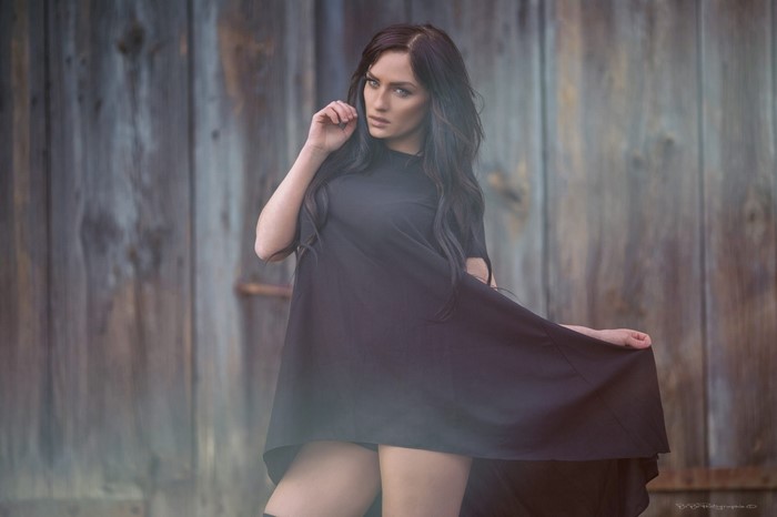 Woman in black dress posing against wooden background