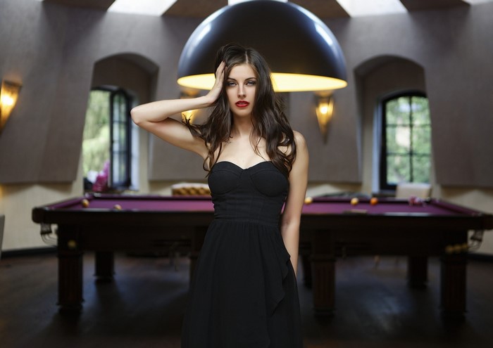 Woman in black dress with hands in hair at pool table