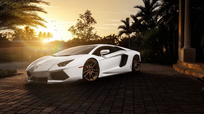 White Lamborghini Aventador parked on cobblestone driveway at sunset
