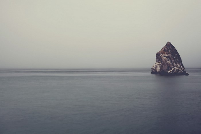 A solitary rock formation in the sea under a foggy sky