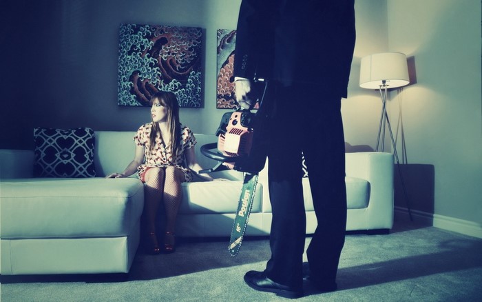 Woman on couch with man holding chainsaw