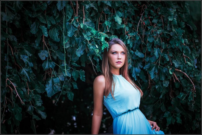 Woman in blue dress posing near green leaves
