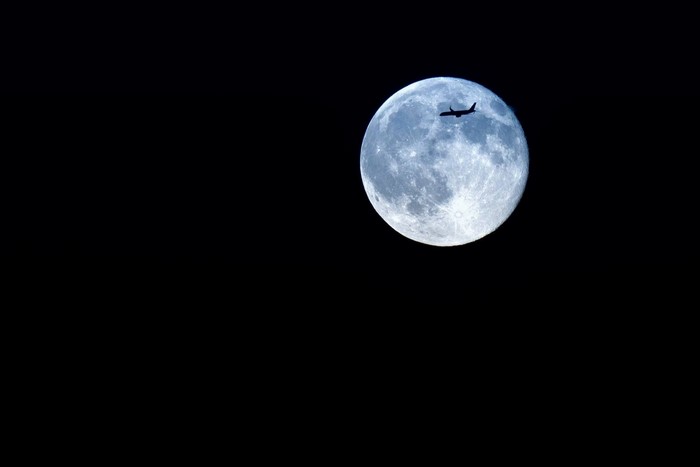Airplane flying in front of a full moon at night