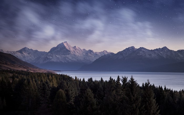 Snowy mountains over a lake at night with stars