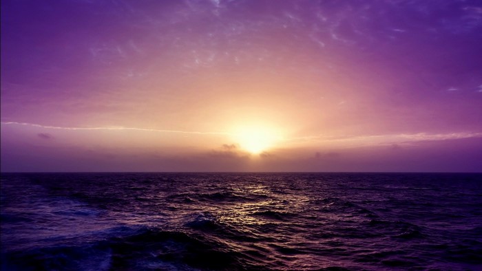 Sunset over the ocean with purple sky and waves