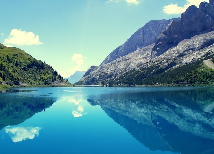 Lake reflecting mountains and green hills under a blue sky