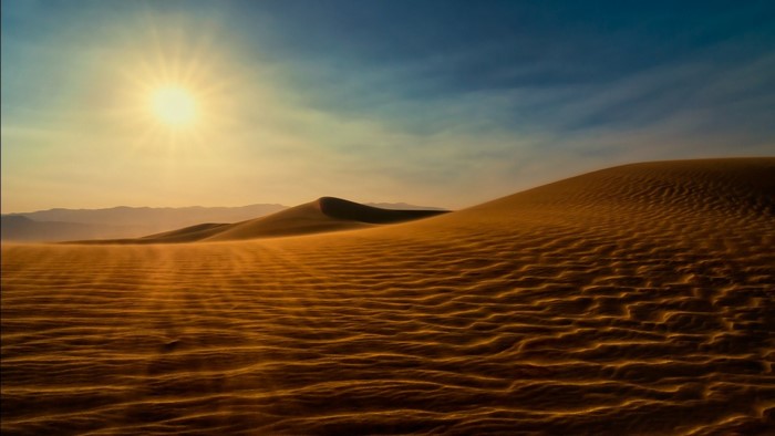 Desert sand dunes at sunset with sun and mountains