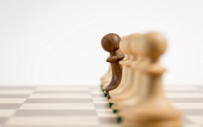 Chess pawns on a chessboard, one dark pawn stands out