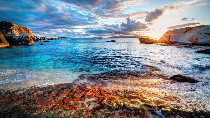 Sailboat on the ocean near rocky shore at sunset