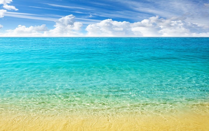Turquoise ocean water meeting a sandy shore under a cloudy blue sky