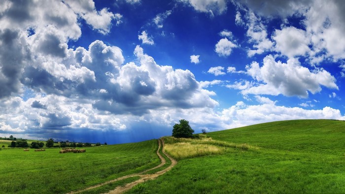 Green rolling hills with a dirt path and dramatic clouds