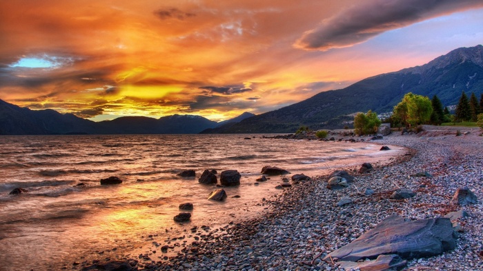 Sunset over a rocky lake shore with mountains