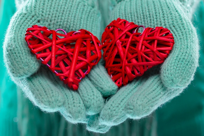 Hands in mittens holding two red heart decorations