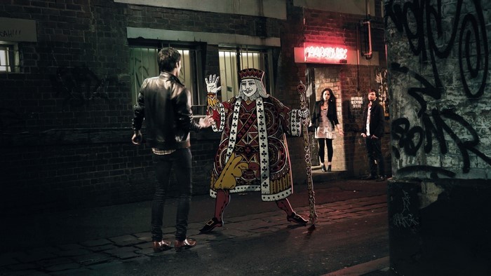 King of Hearts character in an alley with people
