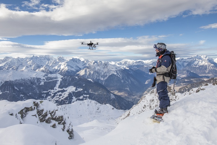 Snowboarder controlling a drone in the Alps