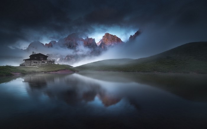 Mountain cabin by a lake with misty peaks at dawn