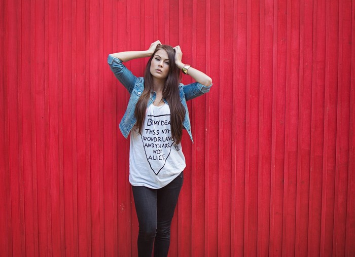 Woman in denim jacket and graphic t-shirt against red wall