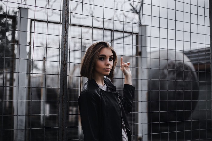 Woman in leather jacket standing by a fence