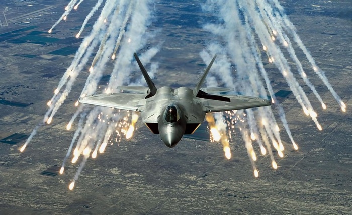 F-22 Raptor releasing flares over a landscape