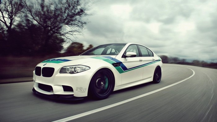 White BMW M5 Sedan with racing stripes driving on a road