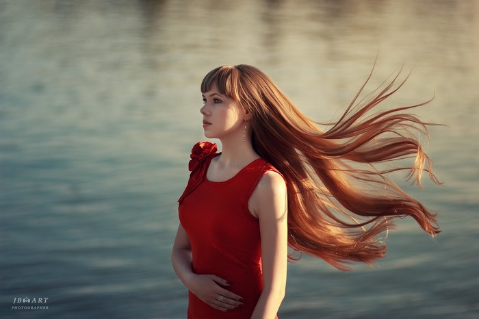 Woman with long red hair in a red dress by the water