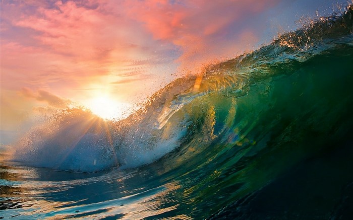 Ocean wave crashing at sunset with sun rays