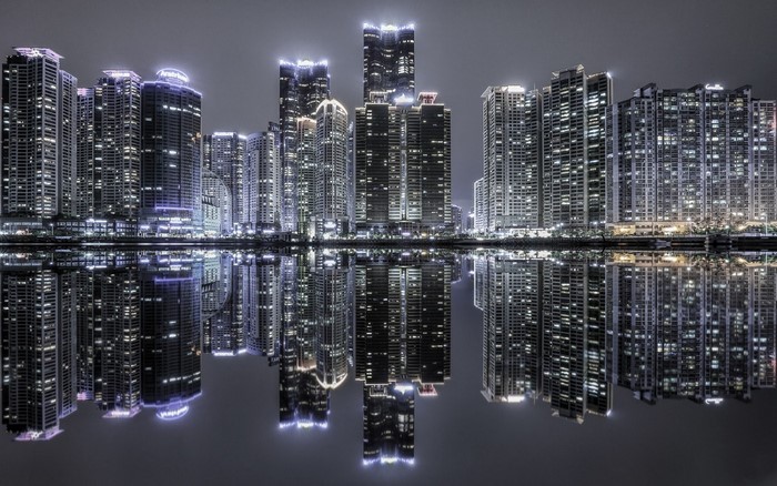 Cityscape with illuminated skyscrapers reflecting in water at night