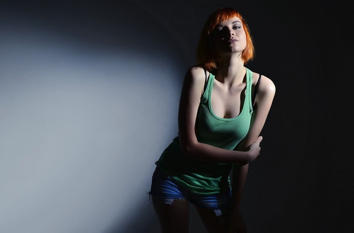 Woman with red hair wearing a green tank top and jean shorts