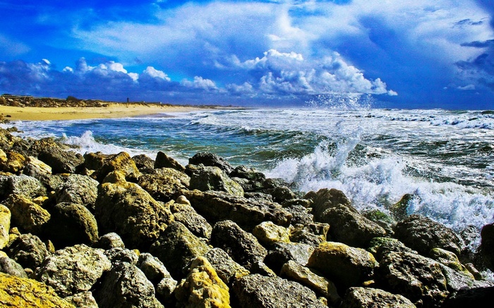 Waves crashing on rocky shore under cloudy blue sky