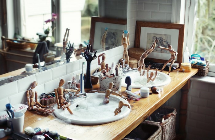 Wooden mannequins playing in a bathroom sink