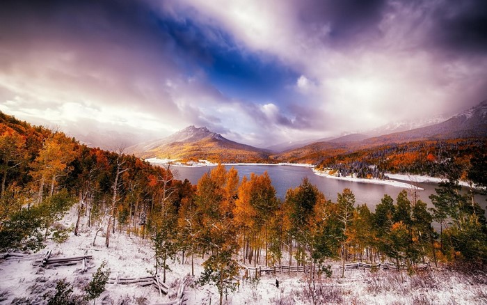 Autumn snow falls on a mountain lake with colorful trees