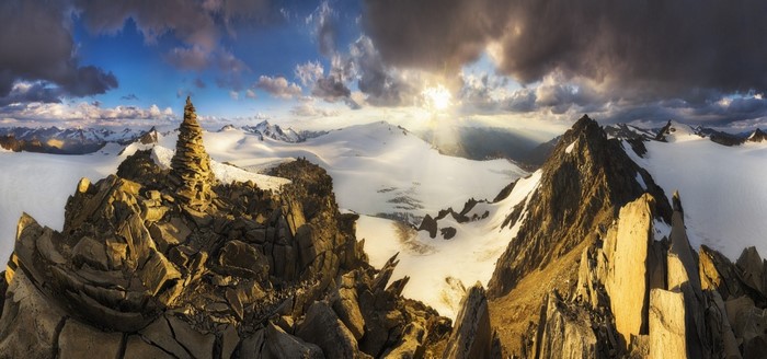Panoramic mountain landscape with sun rays over snow-covered peaks