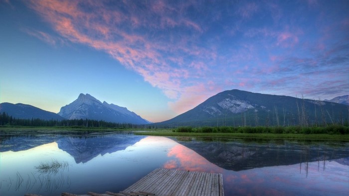 Mountains reflected in a lake at sunrise with a wooden pier