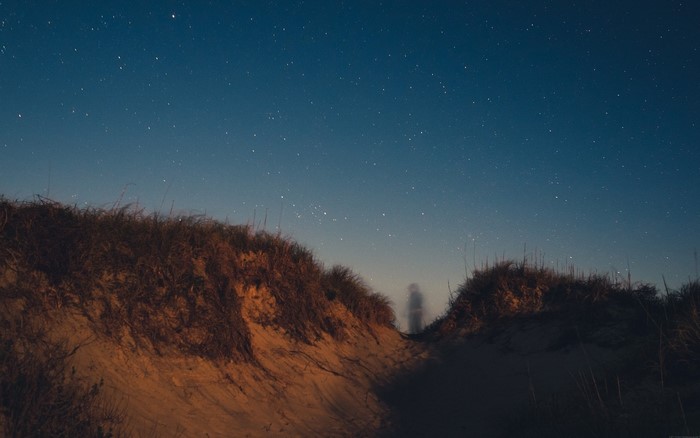 Night sky over sand dunes with faint figure
