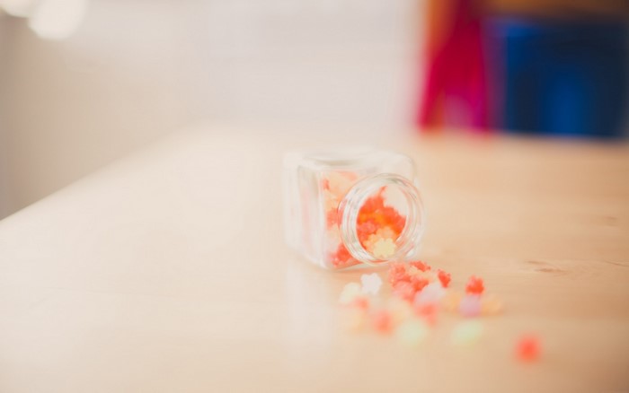 Small glass jar with colorful candies spilled on a wooden table