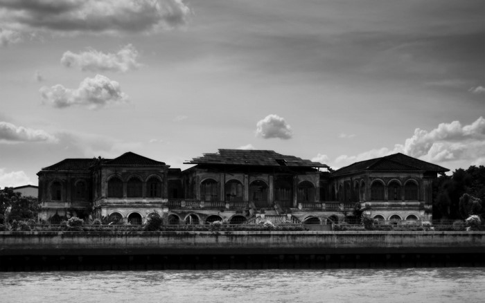 Abandoned mansion on a riverbank under a cloudy sky