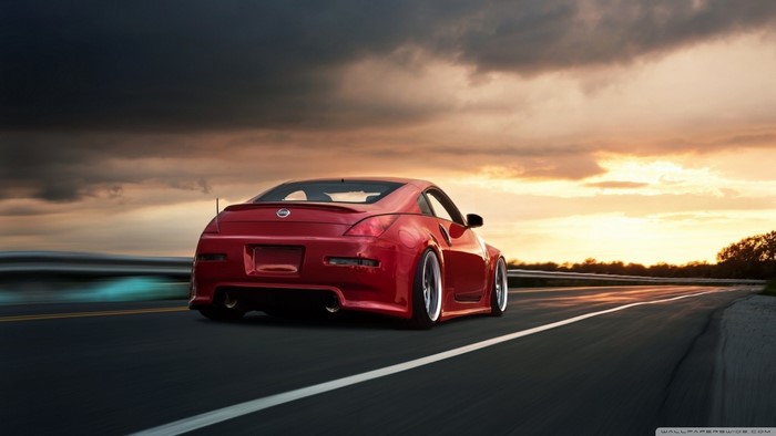 Red Nissan 350Z driving on a road at sunset
