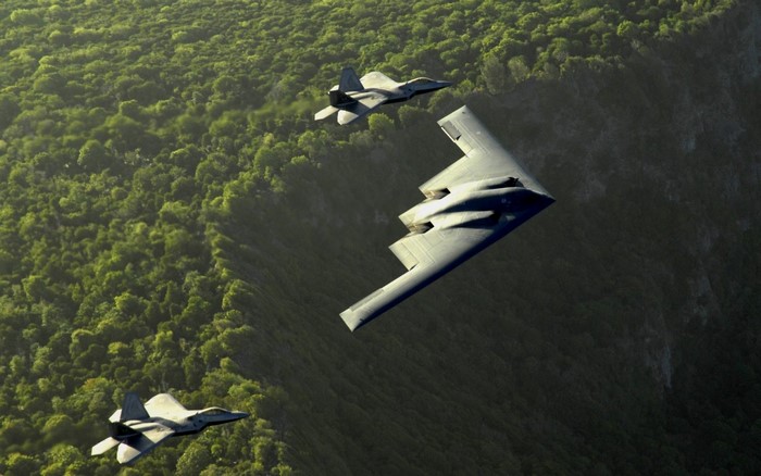 B-2 Spirit and F-22 Raptors flying over forest