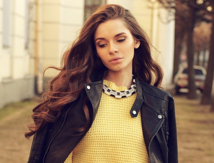 Woman with long brown hair wearing a yellow sweater and leather jacket