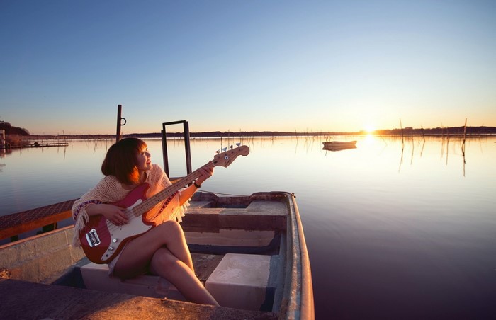 Woman playing bass guitar in a boat at sunset