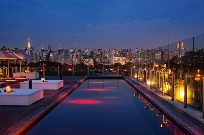 Rooftop swimming pool and lounge area overlooking a city skyline at night