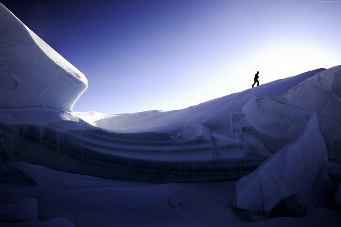 Silhouette of a person walking on a snowy mountain under a clear blue sky