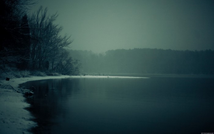 Misty lake with snow-covered trees and forest horizon