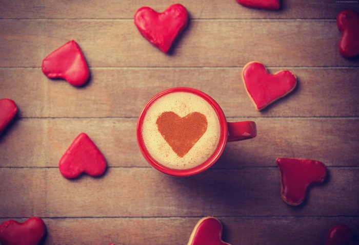 Red coffee cup with heart art surrounded by heart cookies