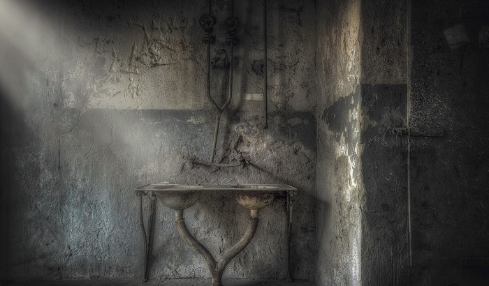 Abandoned room with double sink and pipes