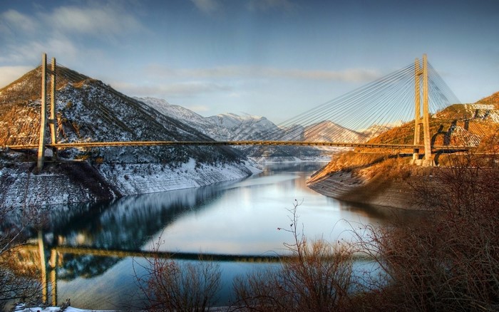 Cable-stayed bridge over a reservoir in a snowy mountain landscape