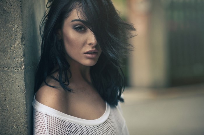 Woman with dark hair leaning against a concrete pillar