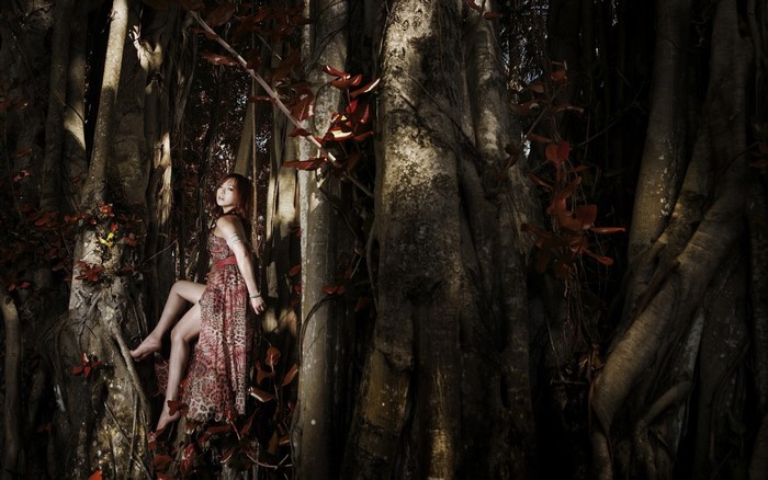 Woman in dress sitting on a tree in a dark forest